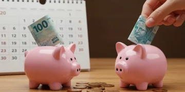 Mão colocando nota de real em cofrinho com calendário de 2025 ao fundo, simbolizando economia mensal.